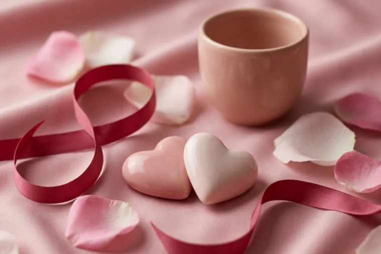A blush mug and two heart-shaped stones among rose petals